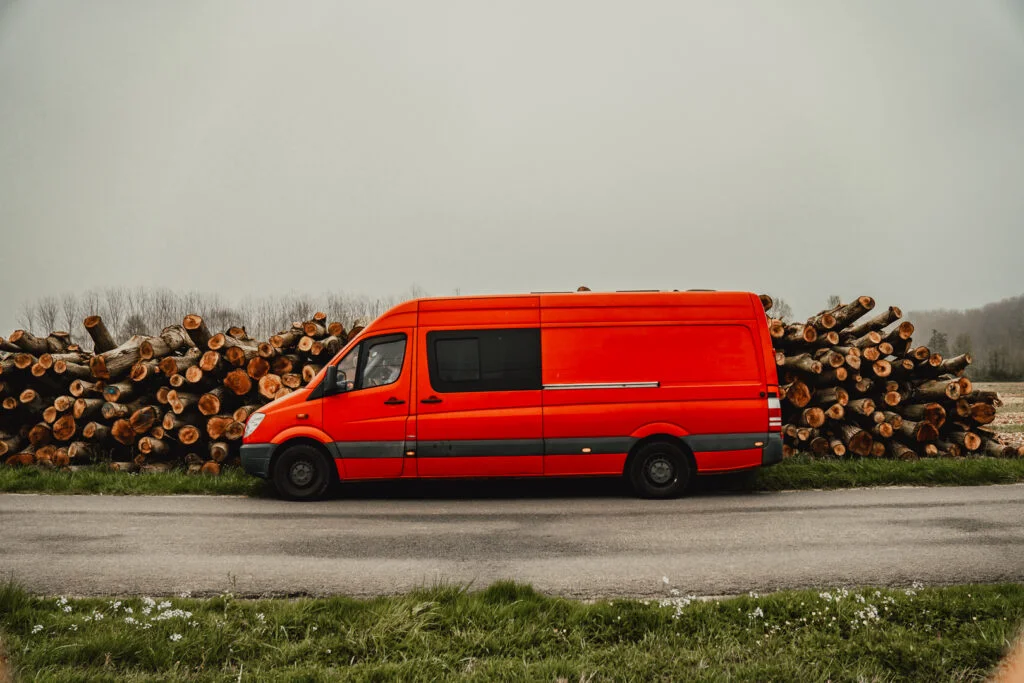 image of a red converted van against logs